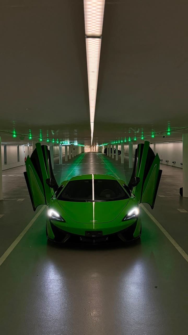 Front view of the Mantis Green McLaren 570S with its dihedral doors open and headlights on