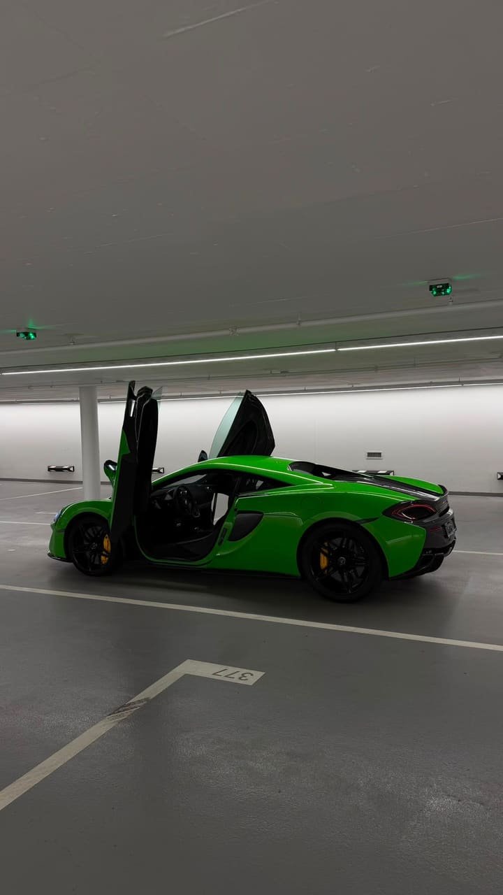 Side view of the green McLaren 570S with an open dihedral door, black wheels and yellow calipers